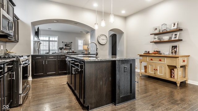 kitchen featuring hanging light fixtures, a center island with sink, sink, light stone countertops, and appliances with stainless steel finishes