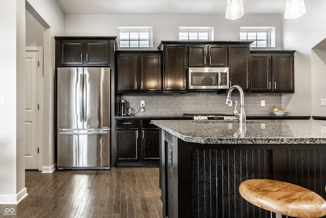 kitchen featuring tasteful backsplash, dark hardwood / wood-style flooring, dark stone countertops, dark brown cabinetry, and stainless steel appliances