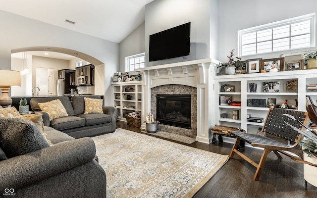 living room featuring a tile fireplace, hardwood / wood-style floors, high vaulted ceiling, and sink