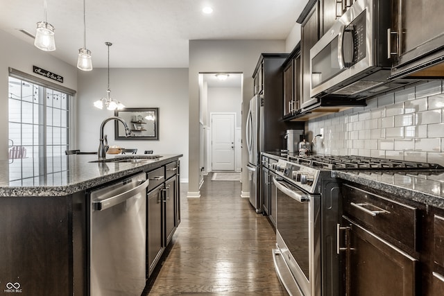 kitchen featuring a kitchen island with sink, hanging light fixtures, sink, appliances with stainless steel finishes, and dark hardwood / wood-style flooring