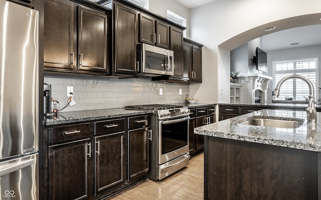 kitchen featuring dark stone counters, sink, dark brown cabinetry, appliances with stainless steel finishes, and light hardwood / wood-style floors