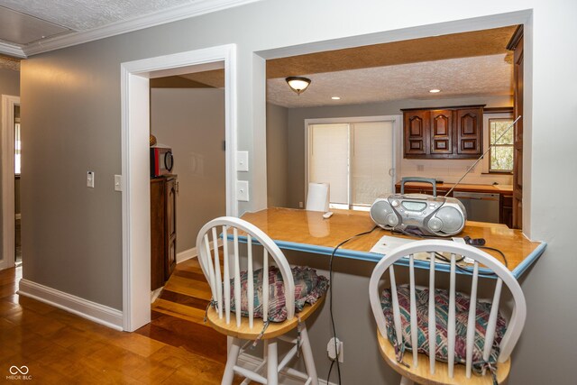 dining space featuring ornamental molding, a textured ceiling, wood finished floors, and baseboards