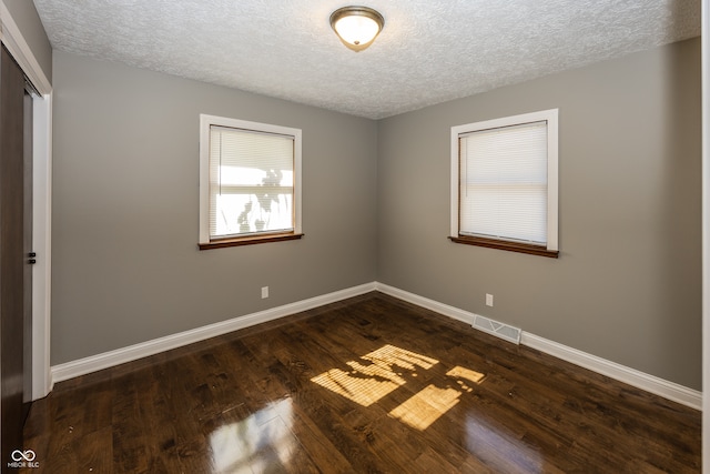 spare room with a textured ceiling and dark hardwood / wood-style flooring