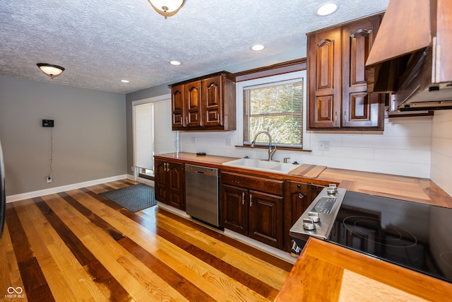 kitchen featuring black appliances, sink, light wood-type flooring, butcher block counters, and a textured ceiling