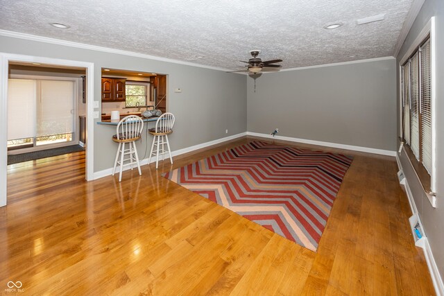 unfurnished living room featuring wood finished floors, a ceiling fan, a textured ceiling, and ornamental molding