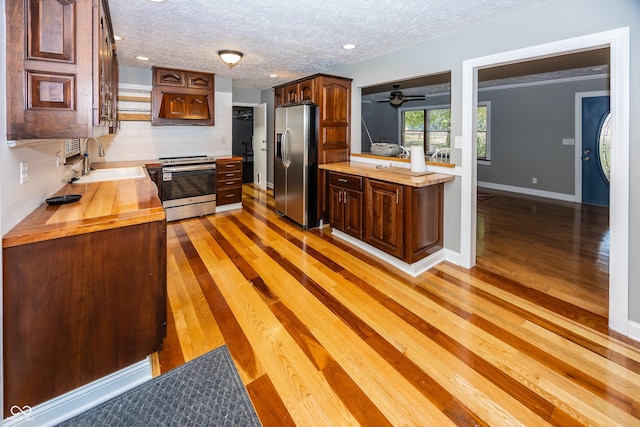 kitchen featuring decorative backsplash, wood counters, light wood-style floors, appliances with stainless steel finishes, and a sink