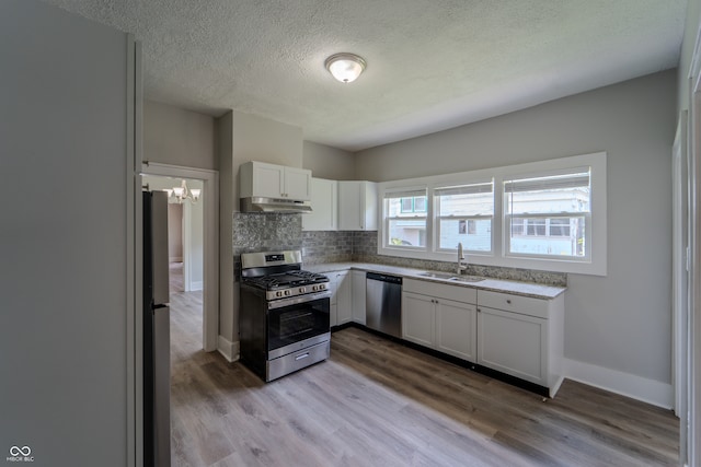 kitchen featuring appliances with stainless steel finishes, sink, backsplash, white cabinets, and hardwood / wood-style flooring