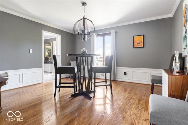 dining space with an inviting chandelier, wood finished floors, wainscoting, and ornamental molding