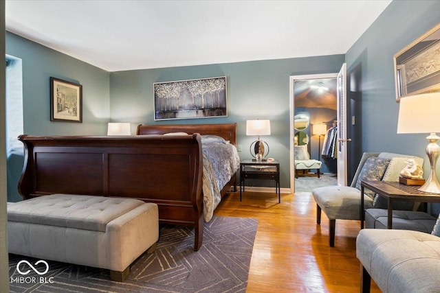 bedroom with a walk in closet, wood finished floors, and baseboards