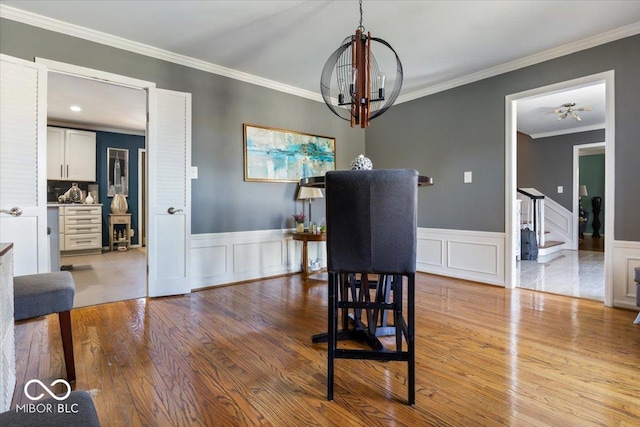 dining area with stairway, wood finished floors, wainscoting, crown molding, and a notable chandelier