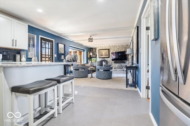 kitchen featuring open floor plan, a breakfast bar, beam ceiling, freestanding refrigerator, and white cabinets