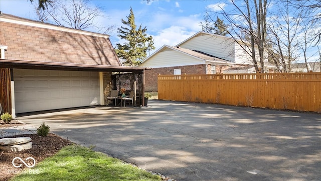 exterior space with driveway, fence, roof with shingles, an attached garage, and brick siding