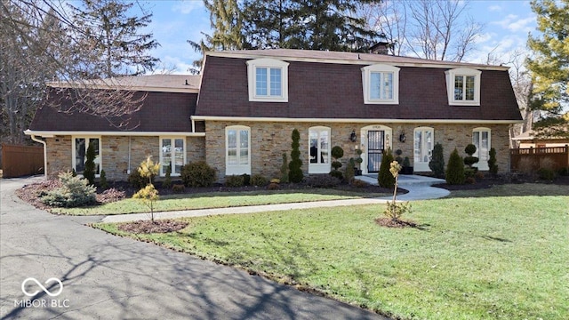 view of front facade featuring mansard roof, stone siding, a front yard, and a shingled roof