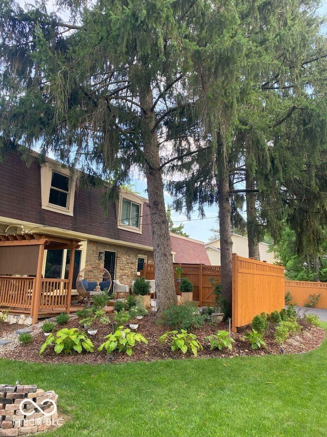 view of front of home with stone siding, roof with shingles, a front lawn, and fence