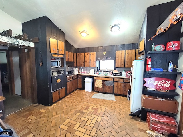 kitchen featuring light parquet flooring, black oven, wooden walls, lofted ceiling, and white refrigerator