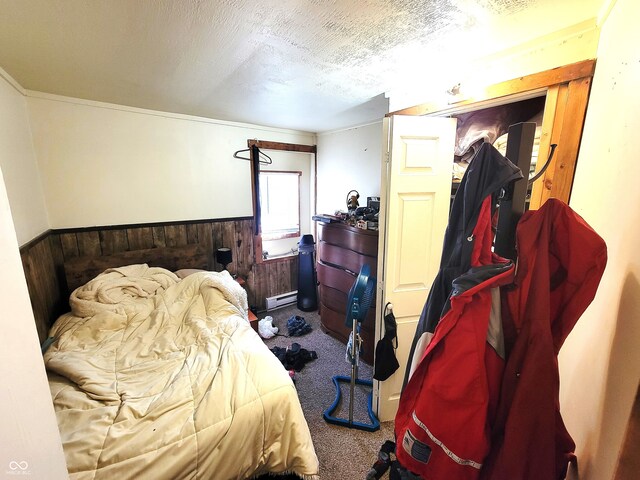 bedroom with wood walls, a textured ceiling, a baseboard radiator, and carpet floors