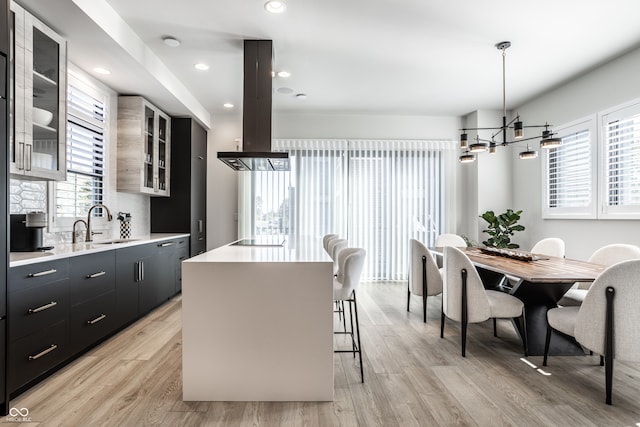 kitchen with a kitchen island, island exhaust hood, hanging light fixtures, a notable chandelier, and light hardwood / wood-style flooring