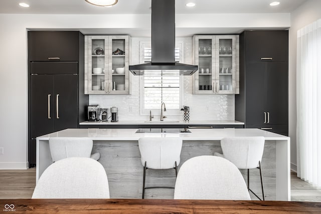 kitchen featuring sink, island range hood, backsplash, a large island, and light hardwood / wood-style flooring