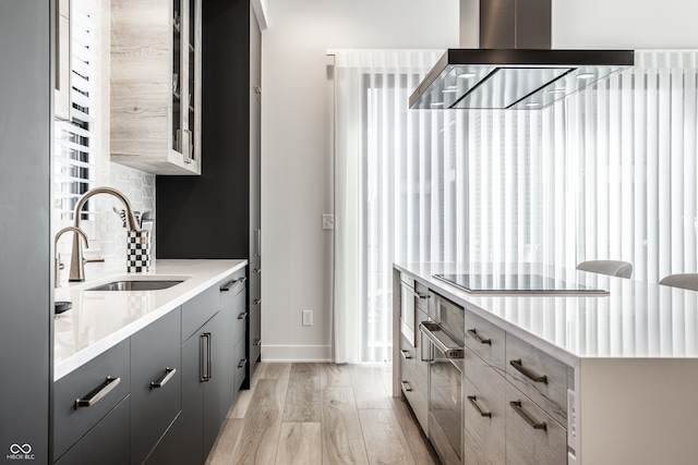 kitchen with sink, black electric cooktop, gray cabinets, light hardwood / wood-style flooring, and exhaust hood