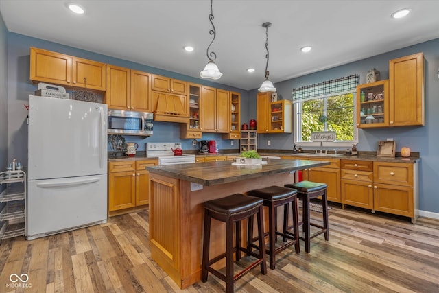 kitchen featuring a breakfast bar area, a kitchen island, light wood-type flooring, decorative light fixtures, and white appliances