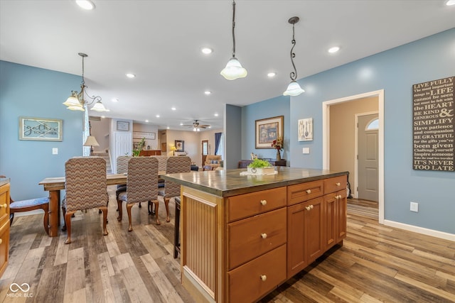 kitchen with light hardwood / wood-style flooring, a center island, hanging light fixtures, and ceiling fan with notable chandelier