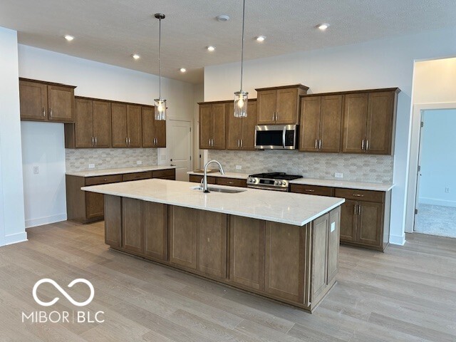 kitchen featuring pendant lighting, sink, stainless steel appliances, a center island with sink, and light wood-type flooring