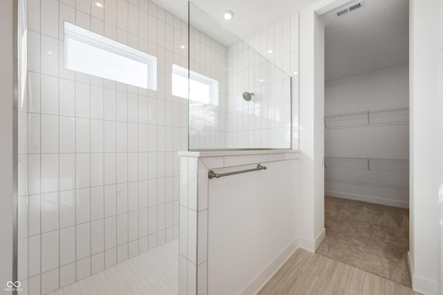 bathroom featuring baseboards, a walk in shower, a walk in closet, and visible vents