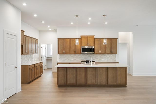 kitchen with brown cabinets, stainless steel microwave, light countertops, hanging light fixtures, and a center island with sink