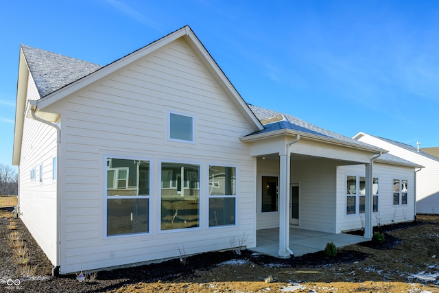 back of property with roof with shingles and a patio