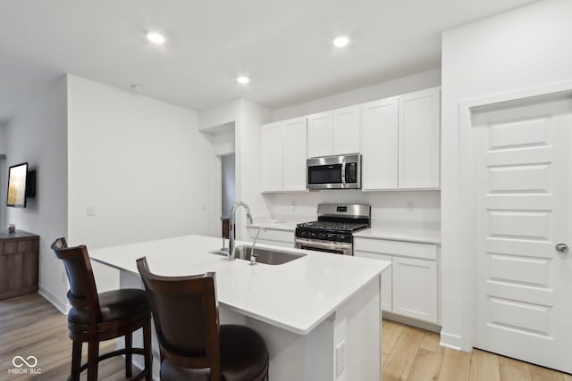 10008 Sundley Dr, Indianapolis, IN 46239 - kitchen with stainless steel appliances, white cabinetry, an island with sink, a sink, and light wood-type flooring