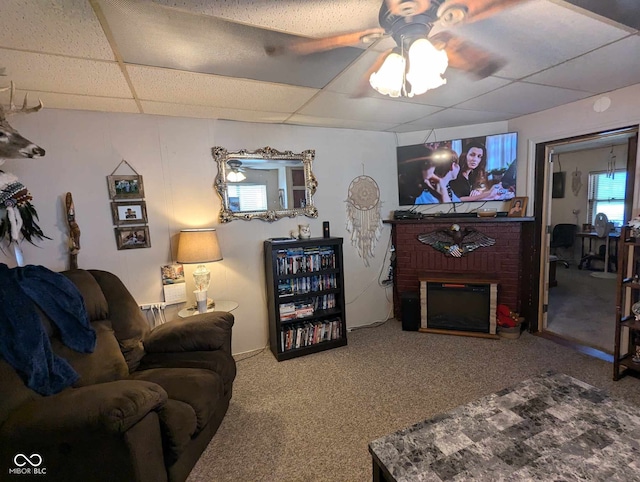 living area featuring carpet floors, a brick fireplace, a drop ceiling, and ceiling fan