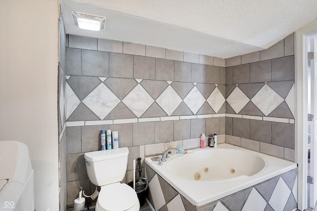 bathroom with toilet, a textured ceiling, tiled tub, and tile walls