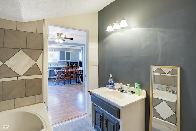 bathroom with a textured ceiling, wood-type flooring, vaulted ceiling, vanity, and a tub to relax in