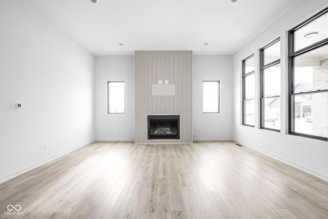 unfurnished living room with a large fireplace, light hardwood / wood-style floors, and a wealth of natural light