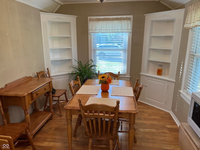 dining area with built in features, wood-type flooring, crown molding, and vaulted ceiling