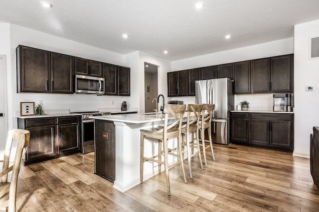 kitchen featuring a kitchen island with sink, a breakfast bar area, dark brown cabinetry, appliances with stainless steel finishes, and light hardwood / wood-style floors