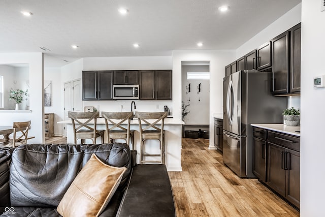 kitchen with a breakfast bar area, appliances with stainless steel finishes, a kitchen island with sink, light hardwood / wood-style flooring, and dark brown cabinetry