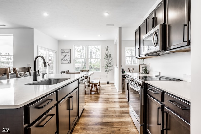 kitchen with a center island with sink, appliances with stainless steel finishes, a textured ceiling, light wood-type flooring, and sink