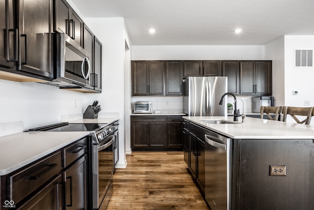 kitchen featuring dark brown cabinets, dark hardwood / wood-style flooring, appliances with stainless steel finishes, a kitchen island with sink, and sink