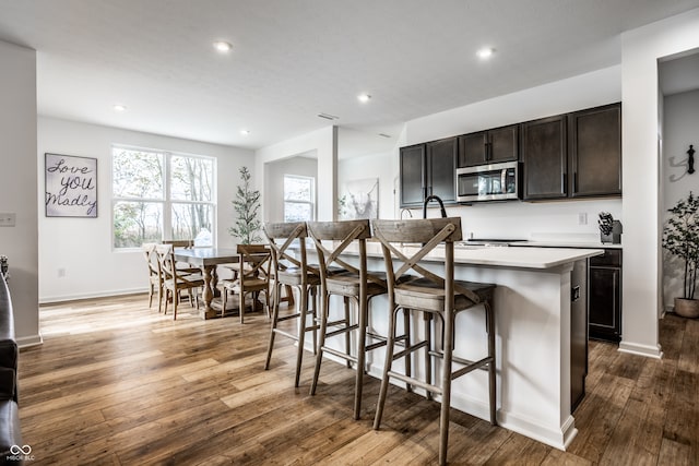 kitchen with dark brown cabinetry, wood-type flooring, a breakfast bar area, and a center island with sink