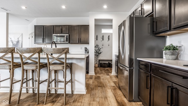 kitchen featuring a breakfast bar area, appliances with stainless steel finishes, dark brown cabinets, and light hardwood / wood-style floors