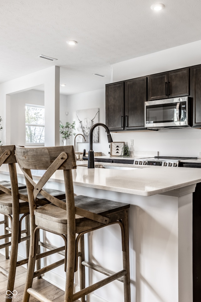 kitchen with a kitchen breakfast bar, light hardwood / wood-style flooring, dark brown cabinets, and a textured ceiling