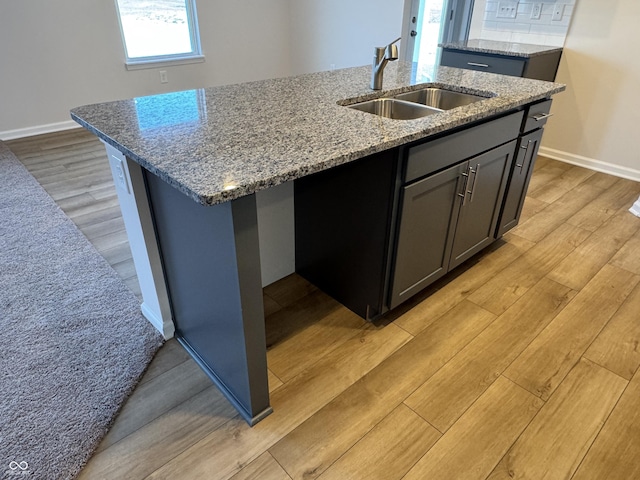 kitchen with a center island with sink, light hardwood / wood-style floors, light stone countertops, and sink