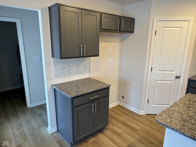 kitchen featuring backsplash, dark stone countertops, gray cabinetry, and light wood-type flooring