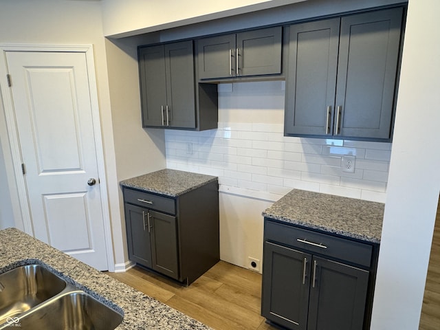 kitchen featuring backsplash, dark stone countertops, sink, and light wood-type flooring