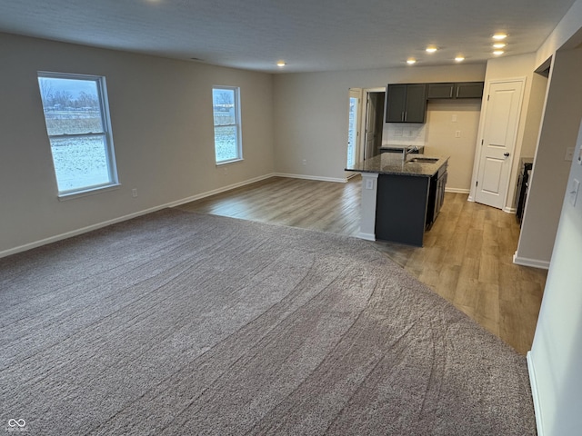 kitchen featuring light wood-type flooring, a center island with sink, dark stone countertops, and sink