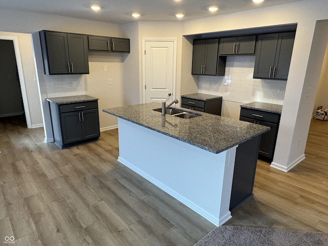 kitchen featuring a center island with sink, wood-type flooring, sink, and tasteful backsplash