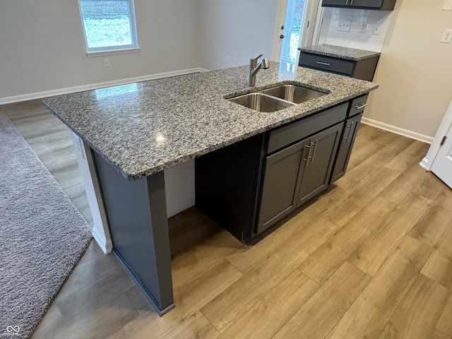 kitchen with stone countertops, light hardwood / wood-style floors, sink, and a kitchen island with sink