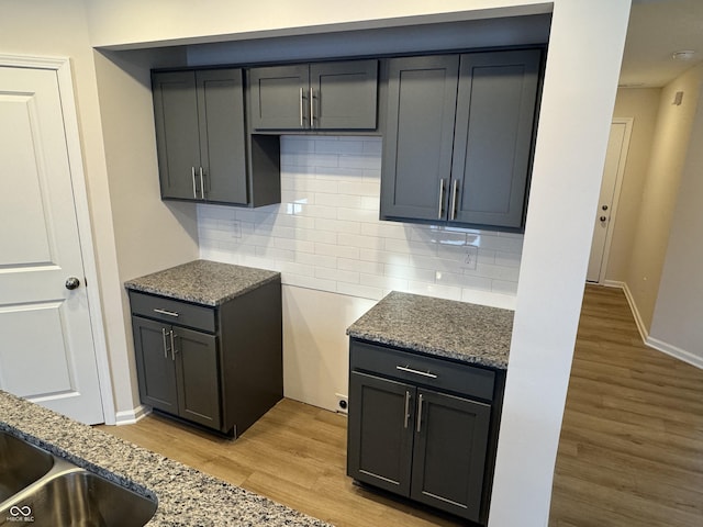 kitchen with light wood-type flooring, tasteful backsplash, and stone countertops