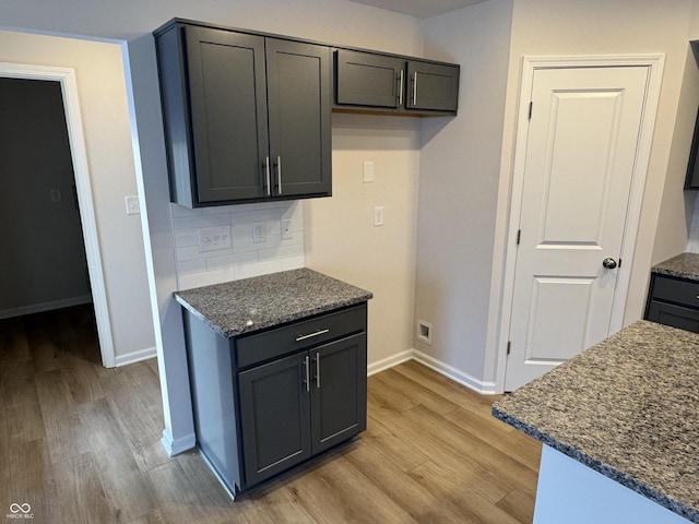 kitchen with backsplash, light hardwood / wood-style flooring, and dark stone counters